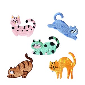 May include: Five embroidered cat patches in various colours. The cats are pink with black spots, blue, green with black spots, brown, and orange with yellow spots. Each patch features a different pose and expression.