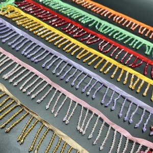 May include: Assortment of beaded fringe trim in various colors, including gold, orange, green, red, yellow, purple, pink, and clear. The fringe is made of small, round beads that are strung together on a thin thread.