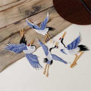 May include: Four embroidered iron-on patches of blue and white cranes with yellow legs. The cranes are in various flying poses.