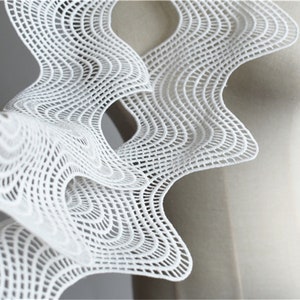 May include: White lace fabric with a geometric pattern. The fabric is draped over a white dress form.