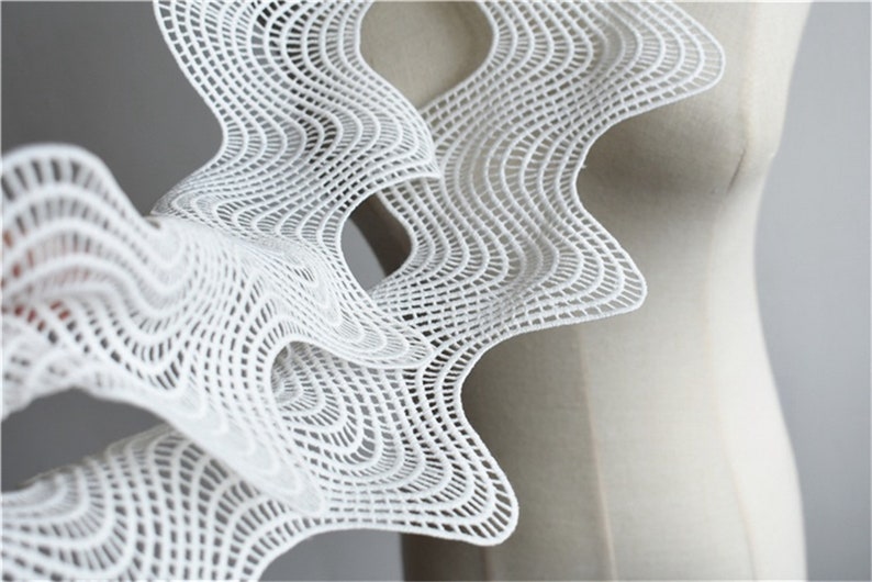 May include: White lace fabric with a geometric pattern. The fabric is draped over a white dress form.