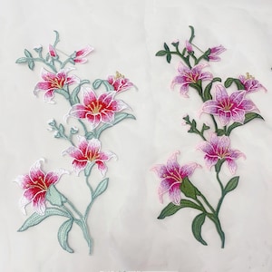 Op de afbeelding: Twee geborduurde leliebloem-patches met levendige roze en witte bloemblaadjes en gele harten. De stengels en bladeren zijn uitgevoerd in groentinten. Elke patch toont een verticale rangschikking van meerdere bloeiende lelies en knoppen.