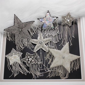 Può includere: Assortimento di sei toppe a forma di stella argentata con frange. Le toppe sono realizzate con paillettes, perline e strass.