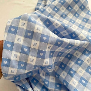 May include: Blue and white gingham fabric with a small heart pattern. The fabric is soft and has a subtle sheen.