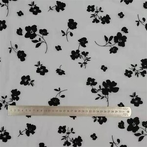 May include: White sheer fabric with a black floral pattern. The fabric is measured with a ruler that shows 30 centimeters.
