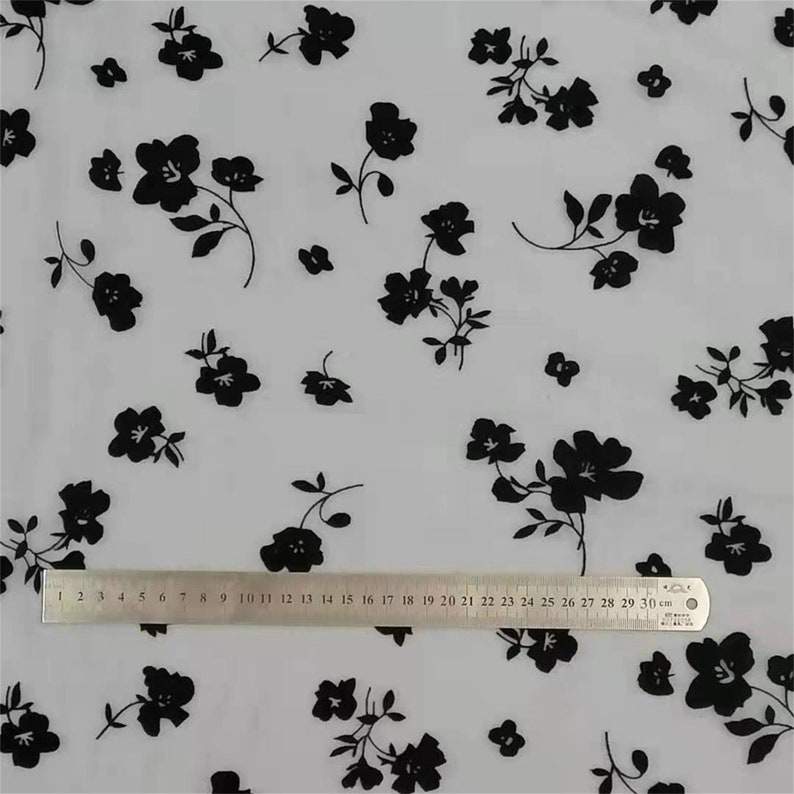 May include: White sheer fabric with a black floral pattern. The fabric is measured with a ruler that shows 30 centimeters.