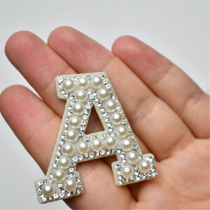 May include: A white felt letter A with a pearl and rhinestone border. The letter is approximately 2 inches tall.