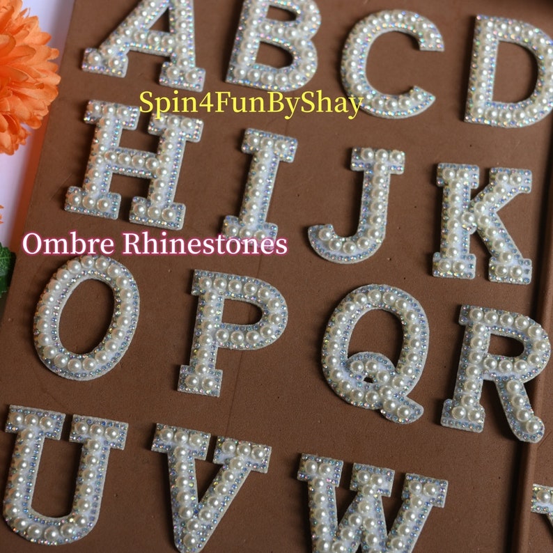 May include: A set of white felt letters decorated with ombre pearl-like rhinestones. The letters are A, B, C, D, H, I, J, K, O, P, Q, R, U, V, and W. The letters are arranged in rows on a brown surface. The text "Spin4FunByShay" and "Ombre Rhinestones" are visible in the image.