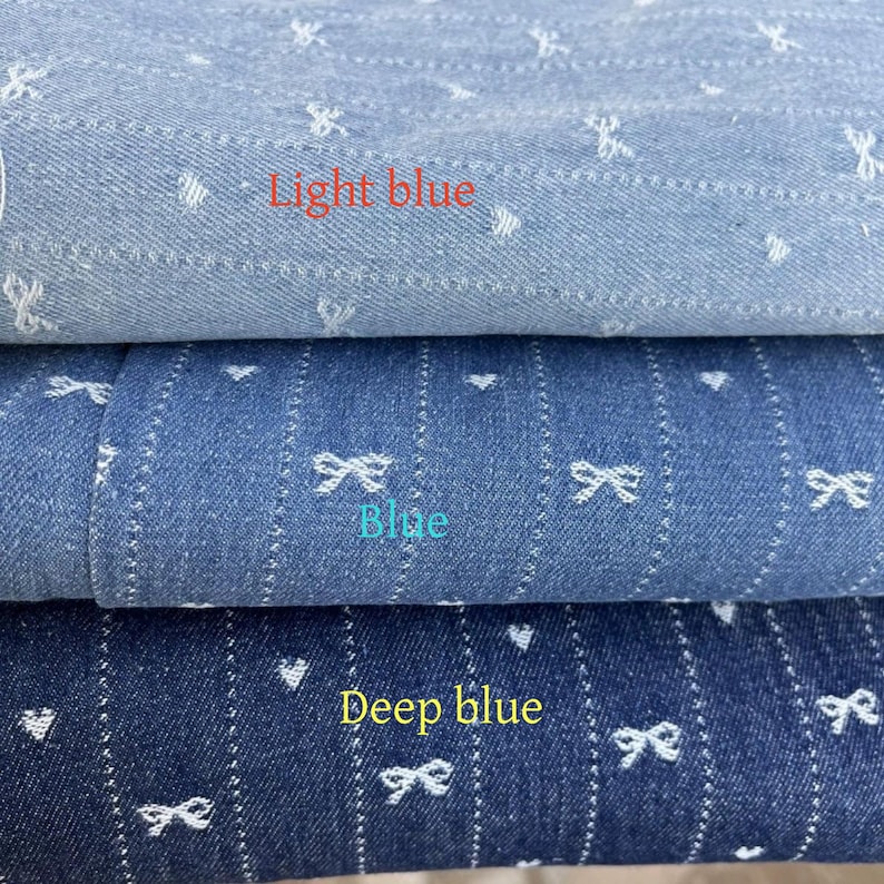 Puede incluir: Tres muestras de tela vaquera con corazones y lazos bordados en blanco. La muestra superior es azul claro, la muestra del medio es azul y la muestra inferior es azul oscuro.