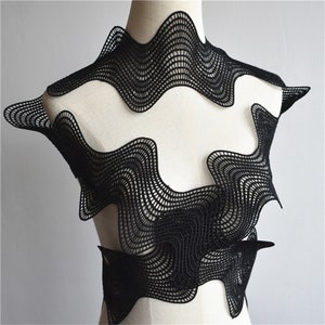 May include: Black lace fabric with a wavy, geometric pattern. The fabric is draped over a white mannequin.