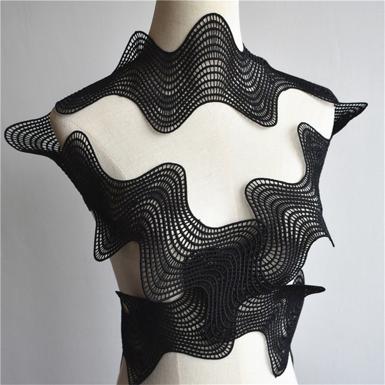 May include: Black lace fabric with a wavy, geometric pattern. The fabric is draped over a white mannequin.
