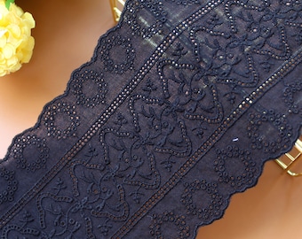 May include: A dark navy blue eyelet lace trim featuring a scalloped edge and a repeating pattern of circular cutouts and intricate embroidered floral motifs arranged in a wide, continuous strip of fabric with a textured finish.