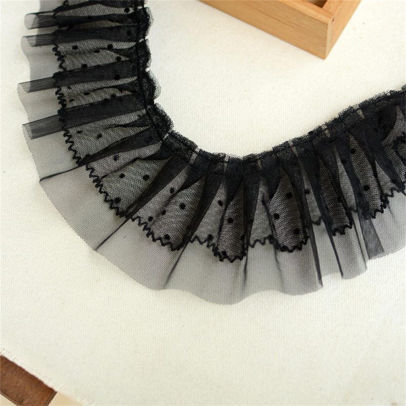 May include: Black lace trim with a dotted pattern. The lace is ruffled and has a delicate, feminine look.