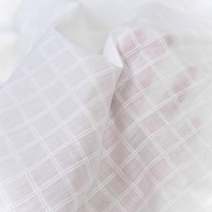 May include: White cotton fabric with a subtle grid pattern. The fabric is soft and lightweight, making it ideal for a variety of sewing projects.