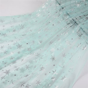 May include: Light blue tulle fabric with silver snowflake and star patterns.