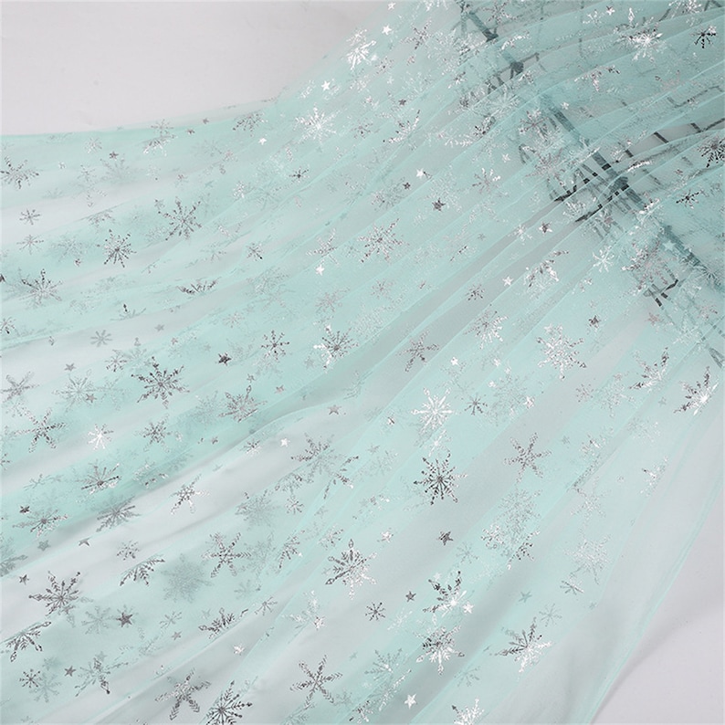 May include: Light blue tulle fabric with silver snowflake and star patterns.