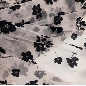 May include: Black floral embroidery on a sheer white fabric. The fabric is delicate and has a soft, flowing texture.