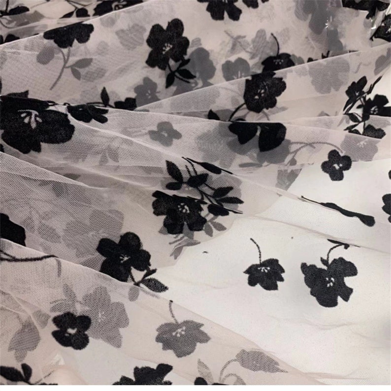 May include: Black floral embroidery on a sheer white fabric. The fabric is delicate and has a soft, flowing texture.
