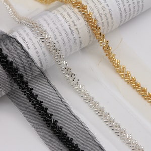 May include: Three different beaded trims on a white background. The trims are black, silver, and gold. The beads are small and rectangular. The trims are all on a mesh backing.