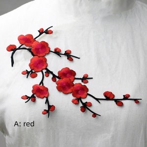 以下が含まれることがあります： 赤い花と蕾が黒い茎に刺繍された花のパッチ。パッチには「A: red」と表示されています。このパッチは布に縫い付けるように設計されています。デザインは花のアクセントです。