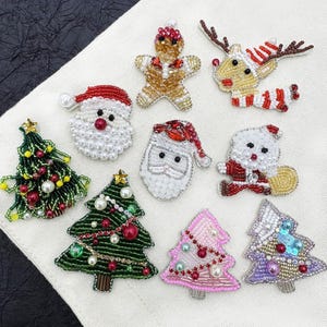 Puede incluir: Una colección de nueve parches de cuentas con temática navideña que incluye un hombre de jengibre, un reno, dos caras de Papá Noel, un Papá Noel de cuerpo entero, dos árboles de Navidad verdes, uno rosa y uno morado con azul.