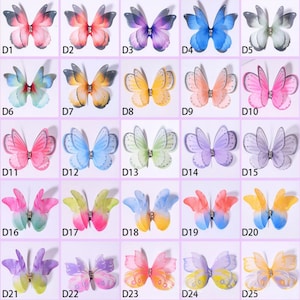 Könnte beinhalten: Eine Sammlung von fünfundzwanzig bunten Schmetterlingsverzierungen. Jeder Schmetterling hat zarte, durchscheinende Flügel in verschiedenen Farbtönen, darunter Rosa, Blau, Lila und Gelb. Die Schmetterlinge sind mit Strasssteinen in der Mitte verziert.