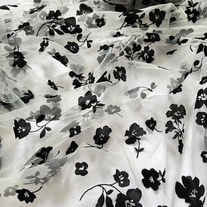 May include: White tulle fabric with black floral embroidery. The fabric is sheer and delicate, with a soft, flowing texture.