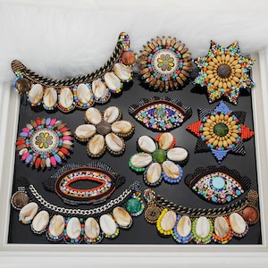 Puede incluir: Una colección de parches de cuentas variados con diversas formas, incluyendo cuellos de media luna, estrellas, flores y ojos. Estos apliques decorativos están elaborados con cuentas de colores, cadenas metálicas y detalles ovalados.