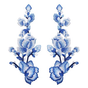 Può includere: Due applicazioni floreali ricamate in blu e bianco con un design delicato. Le applicazioni presentano un gruppo di fiori con un centro bianco e petali blu.