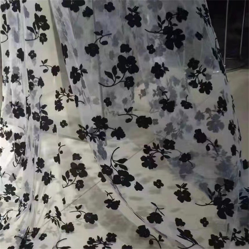 May include: White sheer fabric with a black floral pattern. The fabric is delicate and has a soft, flowing texture.