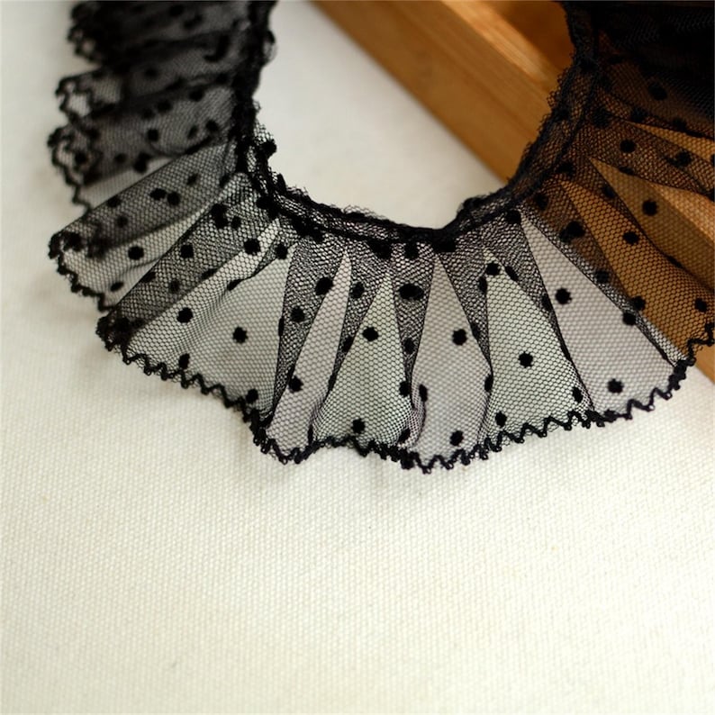 May include: Black lace trim with a scalloped edge and small white polka dots. The lace is gathered and ruffled.