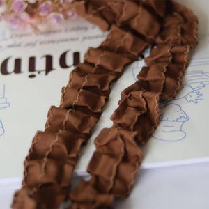 Peut inclure: Garniture à volants marron avec un bord festonné. La garniture est faite d'un tissu doux et souple.