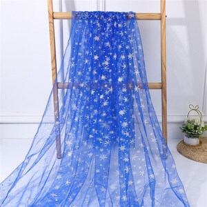 May include: Blue tulle fabric with a white snowflake pattern. The fabric is draped over a wooden ladder.