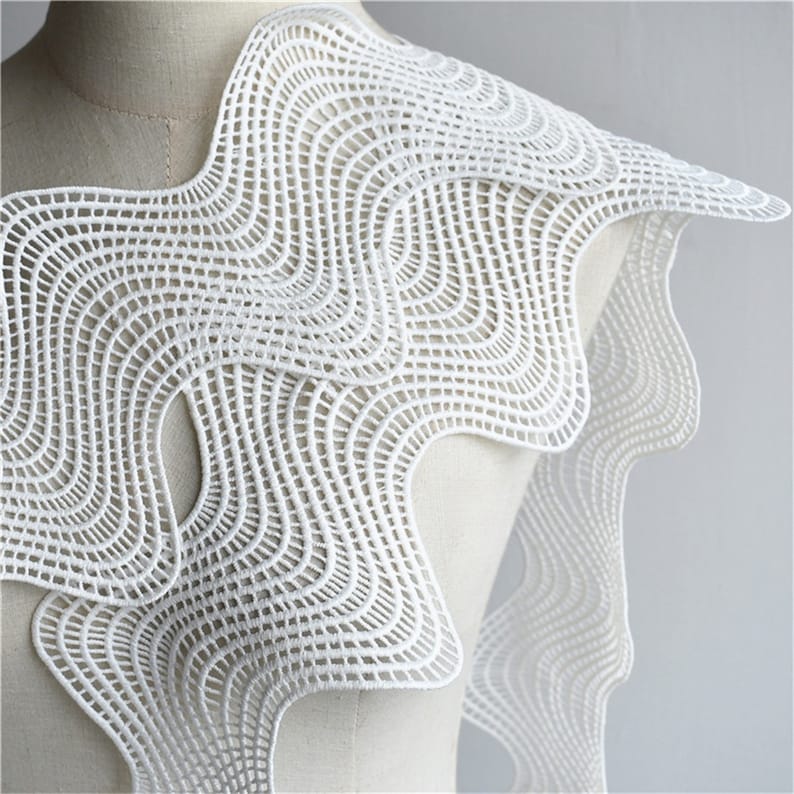 May include: White crocheted lace trim with a wavy, geometric pattern. The lace is delicate and intricate, with a soft, flowing texture.