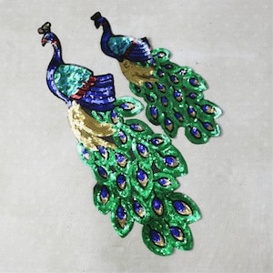 Könnte beinhalten: Zwei Pfauen-förmige Pailletten-Patches in Grün-, Blau- und Goldtönen. Die Patches sind perfekt, um Kleidung, Taschen oder anderen Bastelarbeiten einen Hauch von Glanz zu verleihen.