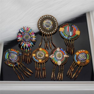May include: Eight colorful beaded and fringed round ornaments with various patterns and designs. The ornaments are made with beads, shells, and feathers.