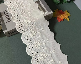 May include: White cotton lace trim with a scalloped edge and delicate floral embroidery. The lace has a subtle sheen and a soft, airy feel.
