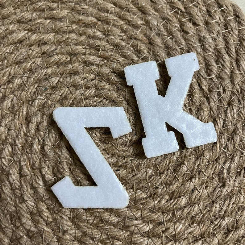 May include: White felt letters, the letter Z and the letter K, on a brown burlap background.
