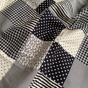 May include: A patchwork quilt featuring various patterns in black and white. Designs include polka dots, stripes, gingham, and floral prints. The quilt is made of soft fabric and has a textured appearance.