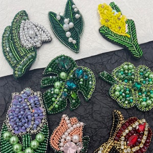 Könnte beinhalten: Sortiment an bunten, bestickten Blumen-Patches mit Perlen und Pailletten. Die Patches zeigen verschiedene Blumenmotive, darunter Lilien, Tulpen und Blätter.