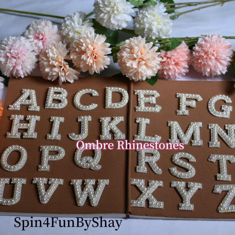 May include: A set of 26 white pearl embellished letters, A through Z, on a brown background. The letters are arranged in two rows, with the text "Ombre Rhinestones" in the middle. The text "Spin4FunByShay" is at the bottom of the image.