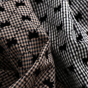 May include: Close-up of a brown and black checkered fabric with a black pattern of small birds. The fabric is folded over, revealing a white and black checkered fabric with a black pattern of small birds.