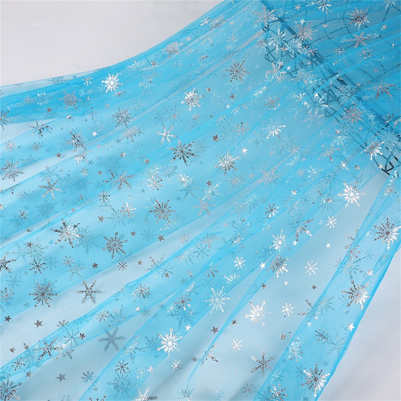 May include: Light blue tulle fabric with silver snowflake and star patterns.