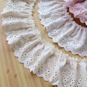 May include: White cotton lace trim with a scalloped edge and delicate floral embroidery. The lace has a gathered look and is perfect for adding a touch of elegance to any project.