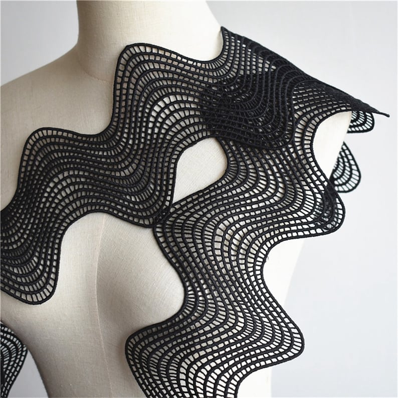 May include: Black lace trim with a wavy, abstract design. The lace is delicate and intricate, with a scalloped edge.
