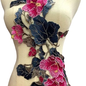 May include: Embroidered floral applique featuring vibrant pink flowers with yellow centers and dark blue leaves. The design is attached to a mannequin, showcasing the intricate details of the craft. Ideal for embellishing garments or accessories.
