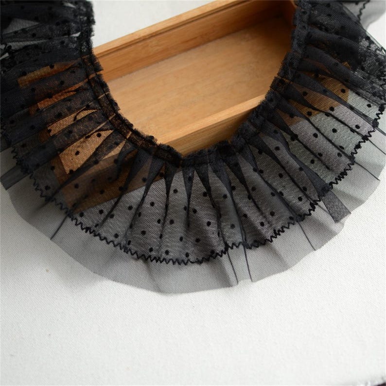 May include: Black lace trim with small white polka dots. The trim is gathered and ruffled, creating a delicate and feminine look.