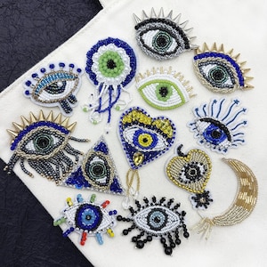 以下が含まれることがあります： 様々な形やサイズの目元をモチーフにした12枚の刺繍ワッペンコレクション。ワッペンはカラフルなビーズ、スパンコール、メタリック糸で装飾されており、ハート、三角形、三日月、様式化された目などのデザインが施されています。