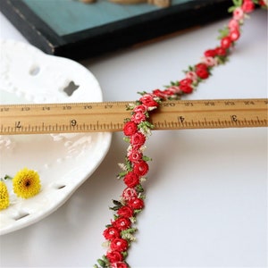 May include: Red and green floral trim with small, embroidered flowers. The trim is measured against a ruler, showing it is approximately 24 inches long.