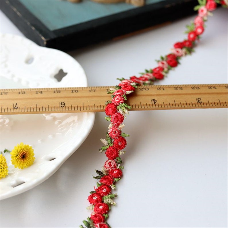 May include: Red and green floral trim with small, embroidered flowers. The trim is measured against a ruler, showing it is approximately 24 inches long.